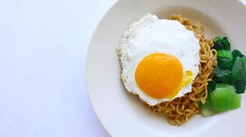 instant noodles served with egg fried and mustard greens on plate. instant fried noodle indomie photo