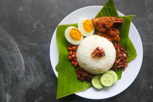 nasi lemak, es un malayo tradicional hecho con huevos cocidos, frijoles, anchoas, salsa de chile, pepino. del plato servido en una hoja de plátano foto