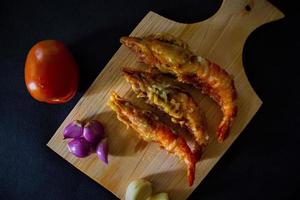 fried shrimp served with tomatoes, shallots, garlic with cutting board on black background photo