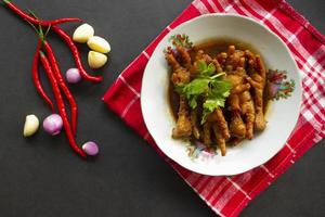 patas de pollo picantes con apio, chile, cebolla, ajo servido con un plato blanco aislado de un fondo negro. foto