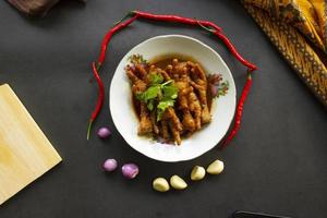 Spicy chicken feet with celery, chili, onion, garlic served with a white plate isolated from a black background. photo
