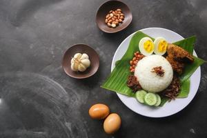 nasi lemak, es un malayo tradicional hecho con huevos cocidos, frijoles, anchoas, salsa de chile, pepino. del plato servido en una hoja de plátano foto