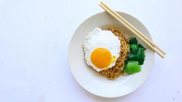 fideos instantáneos servidos con huevo frito y hojas de mostaza en un plato. indomie de fideos fritos instantáneos foto