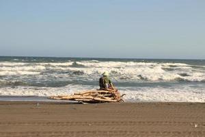 un anciano pescador sentado y pescando en la orilla del mar foto