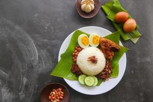 nasi lemak, es un malayo tradicional hecho con huevos cocidos, frijoles, anchoas, salsa de chile, pepino. del plato servido en una hoja de plátano foto