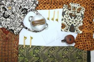 flat lay batik clotes with canting, small pan and wax earthenware glass isolated on white background photo