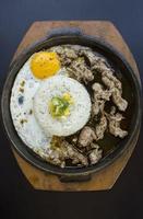 Desayuno con arroz, huevo frito y carne o ternera con guarnición de maíz y puerro en un plato caliente aislado de fondo blanco foto