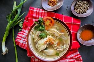Chicken soup served with vegetables, tomatoes, celery in a bowl, spoon and fork. with black background photo