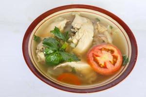 Chicken soup served with vegetables, tomatoes, celery in a bowl, spoon and fork. with black background photo