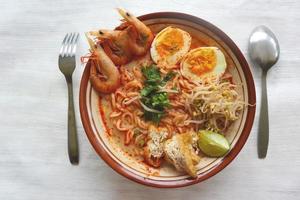 laksa, laksa curry made from vermicelli, noodles, bean sprouts, egg, tofu lime, and shrimp with a spicy soup sauce that is rich in spices. laksa served on bowl, isolated on white background. photo