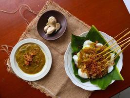 Sate Padang or satay padang is Spicy beef satay from Padang, West Sumatra. Served with spicy curry sauce and rice cake, lontong on banana leaf. isolated on white background photo