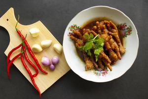 Spicy chicken feet with celery, chili, onion, garlic served with a white plate isolated from a black background. photo