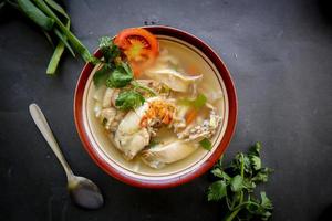 Chicken soup served with vegetables, tomatoes, celery in a bowl, spoon and fork. with black background photo