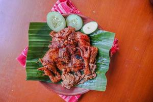 grilled chicken or ayam bakar with cucumber slash served on banana leaf and plate. ayam bakar is traditional grilled chicken from indonesia photo