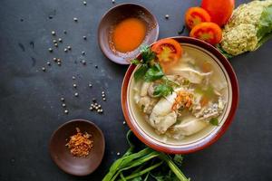Chicken soup served with vegetables, tomatoes, celery in a bowl, spoon and fork. with black background photo