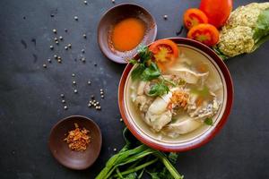 Chicken soup served with vegetables, tomatoes, celery in a bowl, spoon and fork. with black background photo