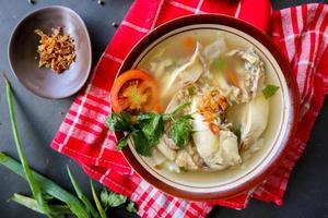 Chicken soup served with vegetables, tomatoes, celery in a bowl, spoon and fork. with black background photo