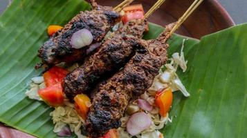 sate buntel o satay buntel es satay hecho de cordero picado envuelto en grasa de cordero y luego asado a la parrilla. condimento con tomates, chalotes, pimienta, repollo foto