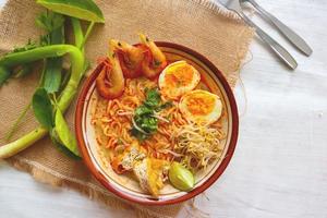 laksa, curry laksa elaborado con fideos, fideos, brotes de soja, huevo, tofu, lima y camarones con una salsa de sopa picante rica en especias. laksa servido en tazón, aislado sobre fondo blanco. foto