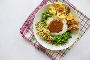 Nasi Pecel or sego pecel is Traditional Javanese rice dish of steamed rice with vegetable salad, peanut sauce, tempeh, tofu bean sprouts and crackers or peyek kacang. on black backgroud photo