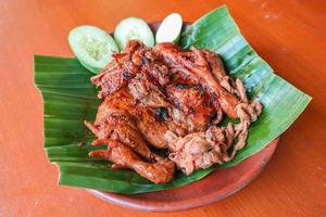 pollo a la parrilla o ayam bakar con pepino servido en hoja de plátano y plato. ayam bakar es pollo asado tradicional de indonesia foto