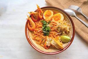 laksa, laksa curry made from vermicelli, noodles, bean sprouts, egg, tofu lime, and shrimp with a spicy soup sauce that is rich in spices. laksa served on bowl, isolated on white background. photo