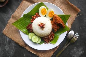 nasi lemak, es un malayo tradicional hecho con huevos cocidos, frijoles, anchoas, salsa de chile, pepino. del plato servido en una hoja de plátano foto