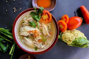 Chicken soup served with vegetables, tomatoes, celery in a bowl, spoon and fork. with black background photo