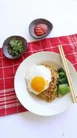 fideos instantáneos servidos con huevo frito y hojas de mostaza en un plato. indomie de fideos fritos instantáneos foto