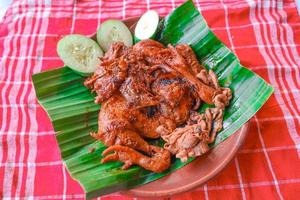 pollo a la parrilla o ayam bakar con pepino servido en hoja de plátano y plato. ayam bakar es pollo asado tradicional de indonesia foto