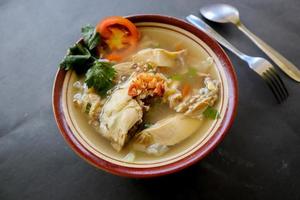 Chicken soup served with vegetables, tomatoes, celery in a bowl, spoon and fork. with black background photo