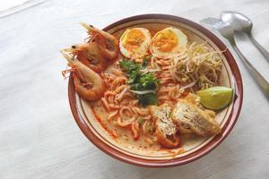 laksa, curry laksa elaborado con fideos, fideos, brotes de soja, huevo, tofu, lima y camarones con una salsa de sopa picante rica en especias. laksa servido en tazón, aislado sobre fondo blanco. foto