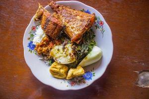 nasi tempong or sego tempong is traditional food from banyuwangi, indonesia made from rice, traditional fried squid, fried eggplant, cucumber slices, vegetables, spinach and spicy sambal  chili photo