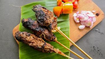 sate buntel o satay buntel es satay hecho de cordero picado envuelto en grasa de cordero y luego asado a la parrilla. condimento con tomates, chalotes, pimienta, repollo foto