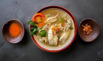 Chicken soup served with vegetables, tomatoes, celery in a bowl, spoon and fork. with black background photo