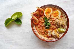 laksa, curry laksa elaborado con fideos, fideos, brotes de soja, huevo, tofu, lima y camarones con una salsa de sopa picante rica en especias. laksa servido en tazón, aislado sobre fondo blanco. foto