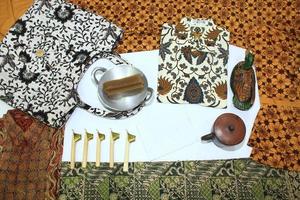 flat lay batik clotes with canting, small pan and wax earthenware glass isolated on white background photo