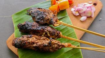 sate buntel o satay buntel es satay hecho de cordero picado envuelto en grasa de cordero y luego asado a la parrilla. condimento con tomates, chalotes, pimienta, repollo foto