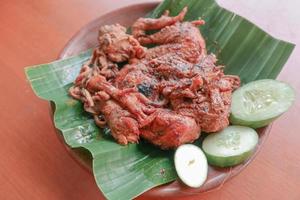 grilled chicken or ayam bakar with cucumber slash served on banana leaf and plate. ayam bakar is traditional grilled chicken from indonesia photo