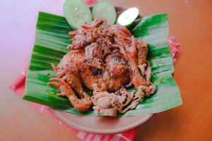 pollo a la parrilla o ayam bakar con pepino servido en hoja de plátano y plato. ayam bakar es pollo asado tradicional de indonesia foto