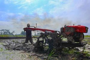 farmer plowing muddy field with hand tractor on indonesia, asia photo