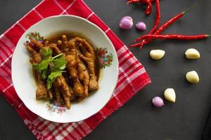 patas de pollo picantes con apio, chile, cebolla, ajo servido con un plato blanco aislado de un fondo negro. foto