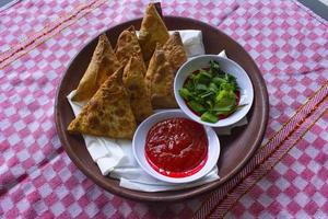 samosa, samsa o somsa son pasteles fritos triangulares o pastri servidos con salsa de tomate y rodaja de puerro, sobre fondo negro foto