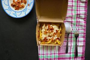 fried fries with with melted cheddar cheese or fried cheese with topping sausage slices on box photo