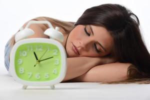 Beautiful sleeping woman resting in bed with alarm clock ready to wake her in the morning. photo