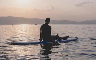 Sporty young man on SUP paddle board going to the sea at sunset. photo