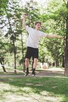 Young man balancing and jumping on slackline. Man walking, jumping and balancing on rope in park. photo