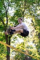 Young man balancing and jumping on slackline. Man walking, jumping and balancing on rope in park. photo