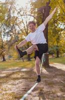 Young man balancing and jumping on slackline. Man walking, jumping and balancing on rope in park. photo