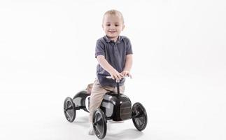 Little boy riding Retro style toy car. Boy riding old metal pedal car for children from the 19th century. photo